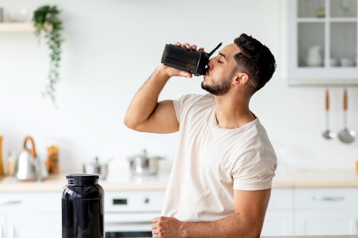  A man drinks from a black shaker, likely containing creatine for his workout routine.
