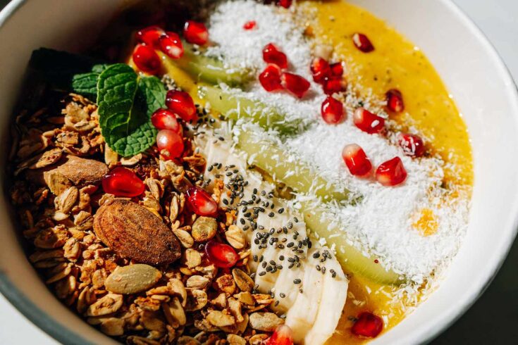 A colorful bowl of mixed fruit, nuts, and granola, with a spoon resting beside it, ideal for a nutritious meal.