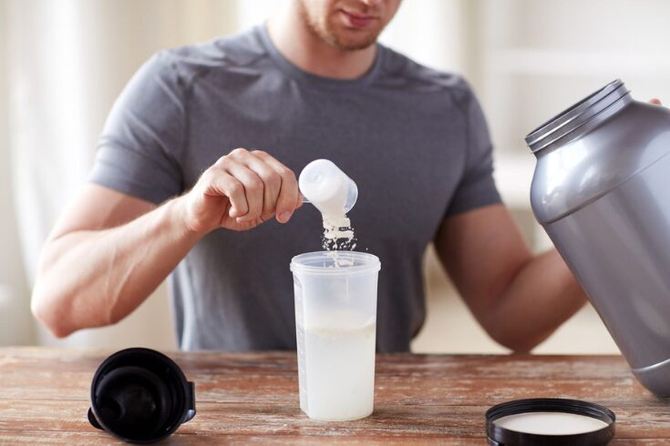  A man is carefully pouring a liquid supplement, creatine, into a transparent bottle for mixing.