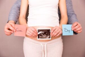 Pregant woman holding ultrasound image of baby, with husband holding boy & girl notes