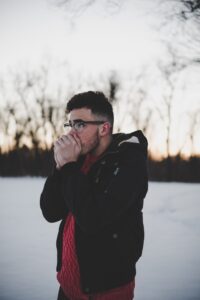 Man in snowy weather, blowiing hot air into hands to keep warm